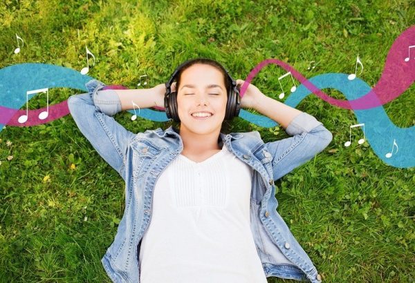 lifestyle, summer vacation, technology, music and people concept - smiling young girl in headphones lying with closed eyes on grass